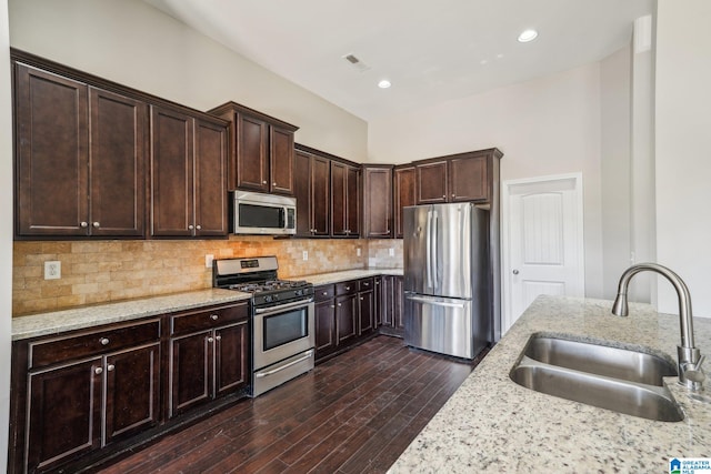 kitchen featuring dark brown cabinetry, sink, stainless steel appliances, light stone counters, and dark hardwood / wood-style flooring