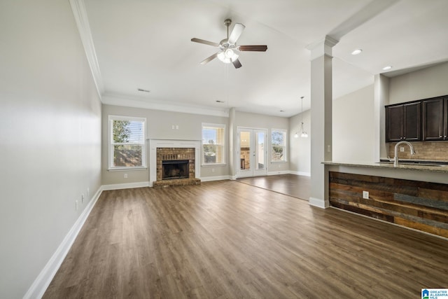 unfurnished living room with ceiling fan, sink, dark wood-type flooring, a brick fireplace, and crown molding