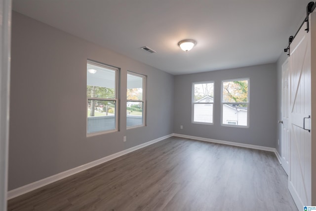 empty room featuring a barn door, plenty of natural light, and dark hardwood / wood-style floors