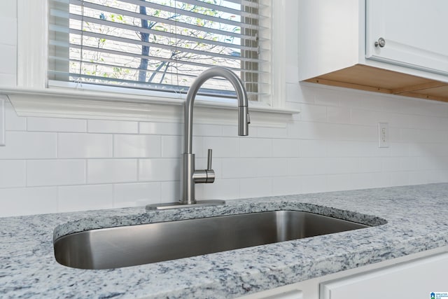 room details with white cabinets, decorative backsplash, light stone countertops, and sink