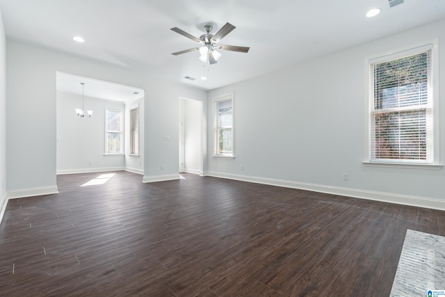 empty room featuring a wealth of natural light, dark wood-type flooring, and ceiling fan with notable chandelier