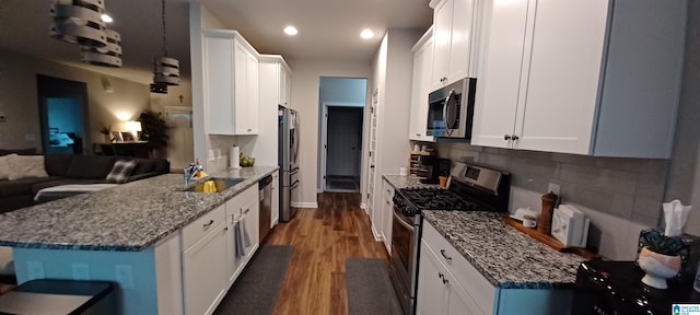 kitchen featuring dark wood-style flooring, appliances with stainless steel finishes, white cabinets, a sink, and dark stone countertops