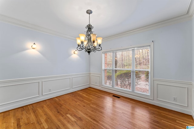 spare room with hardwood / wood-style flooring, an inviting chandelier, and crown molding