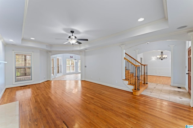 unfurnished living room with a tray ceiling, crown molding, light hardwood / wood-style floors, and ceiling fan with notable chandelier