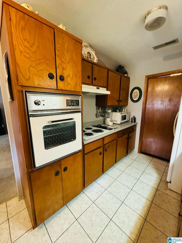 kitchen with a textured ceiling, light tile patterned floors, and white appliances