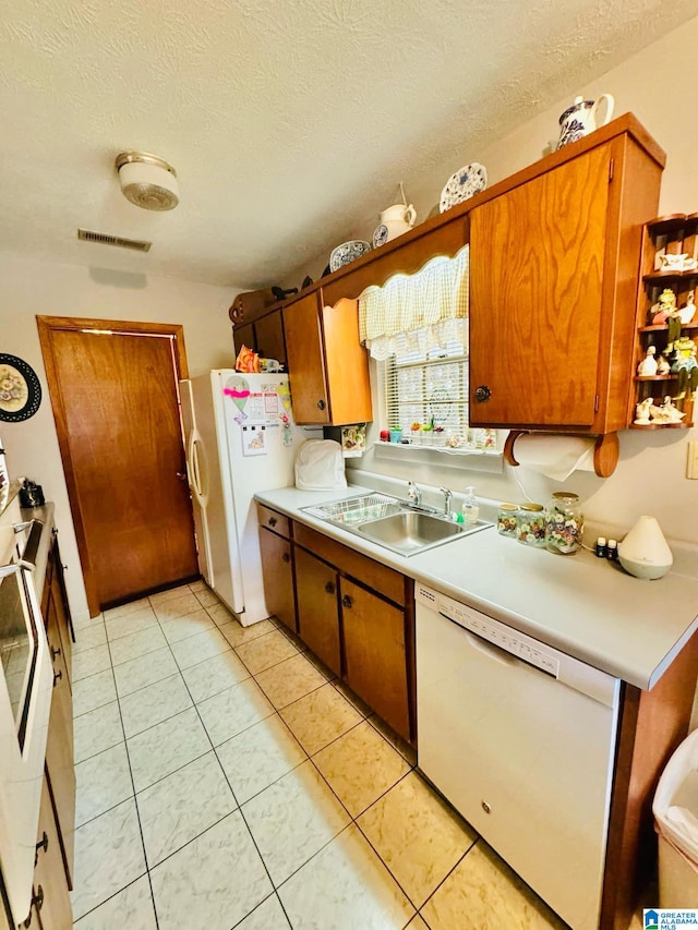 kitchen featuring a textured ceiling, white appliances, sink, and light tile patterned floors