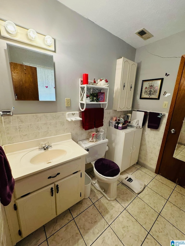 bathroom with vanity, tile patterned floors, toilet, a textured ceiling, and tile walls