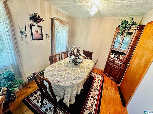 dining space with wood-type flooring, a textured ceiling, baseboard heating, and plenty of natural light