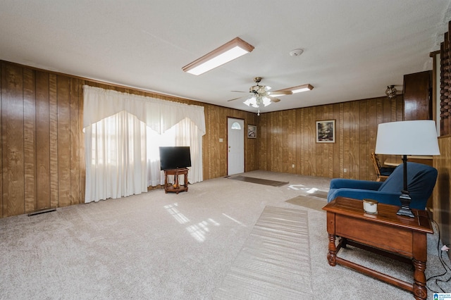 carpeted living room with ceiling fan and wood walls