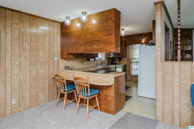 kitchen with sink, kitchen peninsula, wood walls, white fridge, and black stovetop