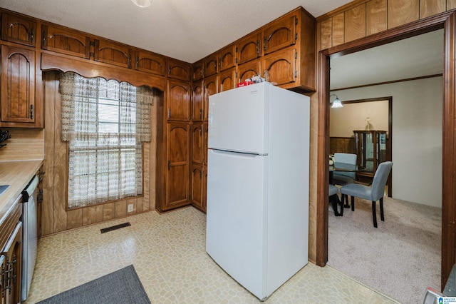 kitchen featuring dishwasher, wood walls, white refrigerator, a textured ceiling, and light colored carpet