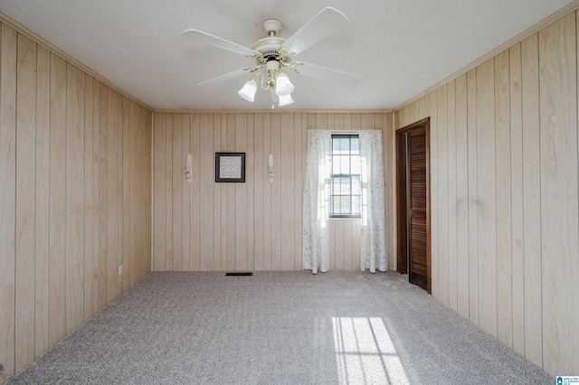 carpeted empty room featuring wooden walls and ceiling fan