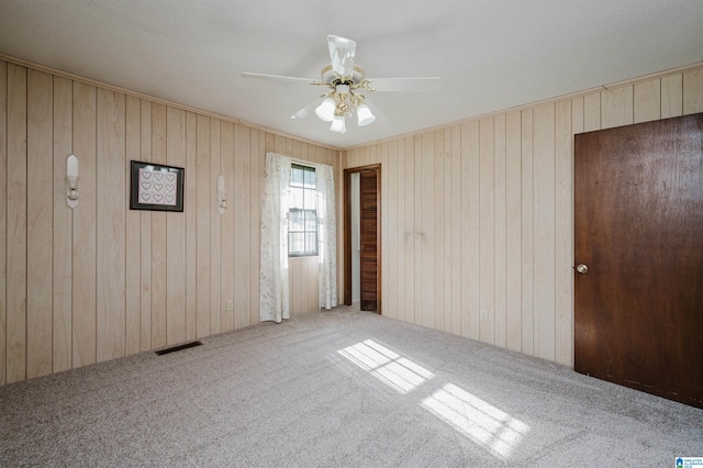 carpeted empty room featuring ceiling fan and wooden walls