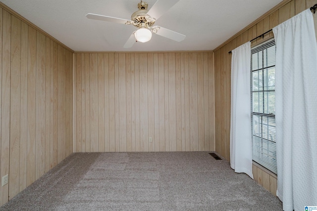 unfurnished room with carpet flooring, ceiling fan, and wood walls