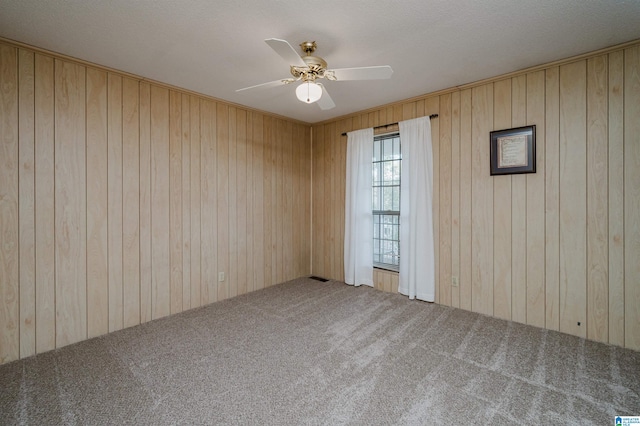 spare room with wood walls, carpet, and ceiling fan