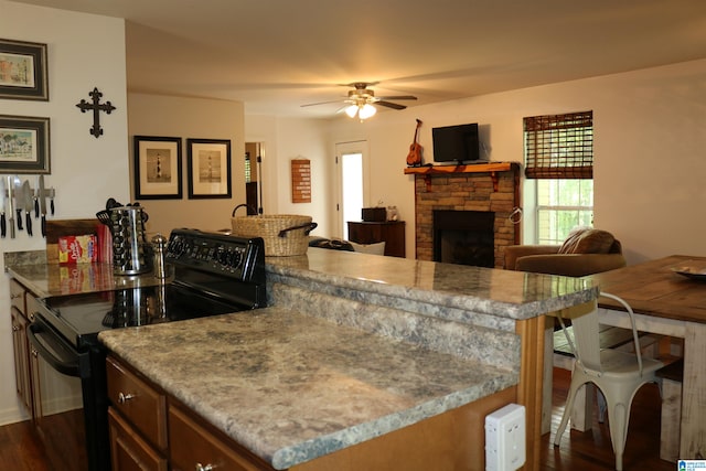 kitchen with light stone countertops, dark hardwood / wood-style flooring, ceiling fan, electric range, and a stone fireplace