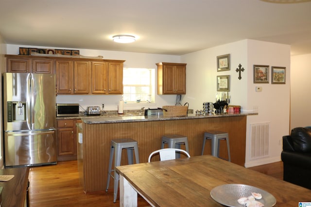 kitchen with kitchen peninsula, a kitchen breakfast bar, stainless steel appliances, dark stone countertops, and light hardwood / wood-style floors