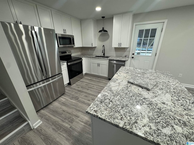 kitchen featuring pendant lighting, light hardwood / wood-style flooring, light stone countertops, white cabinetry, and stainless steel appliances