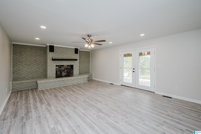 unfurnished living room with french doors, a brick fireplace, ceiling fan, light hardwood / wood-style floors, and brick wall