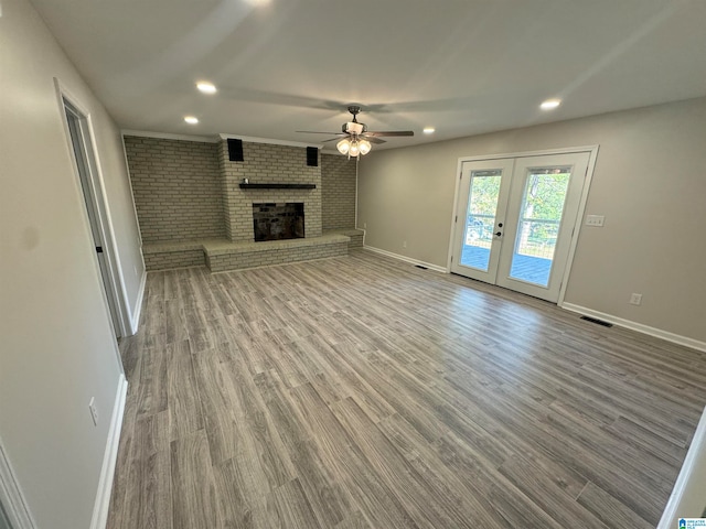 unfurnished living room featuring ceiling fan, a fireplace, wood-type flooring, and french doors