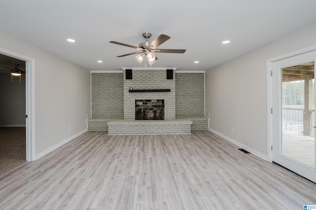 unfurnished living room featuring ceiling fan, a fireplace, light hardwood / wood-style floors, and brick wall