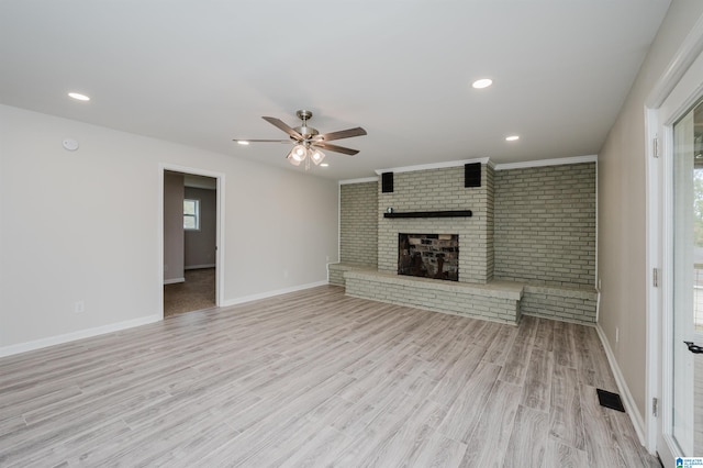 unfurnished living room with a fireplace, light hardwood / wood-style floors, ceiling fan, and brick wall