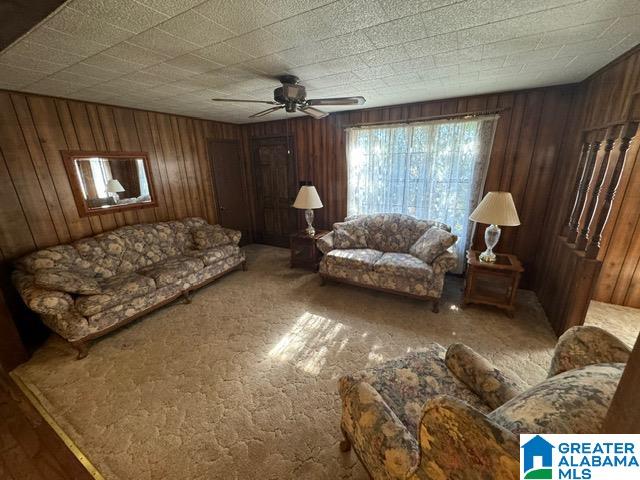 living room with wooden walls, carpet floors, and ceiling fan