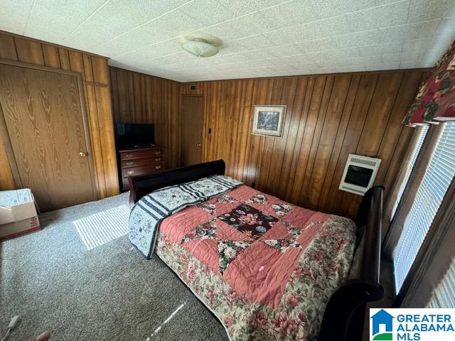 carpeted bedroom with heating unit and wood walls