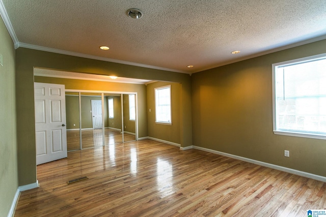 empty room featuring crown molding, light hardwood / wood-style floors, and a textured ceiling