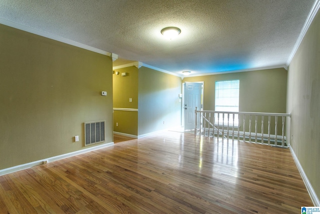 empty room featuring a textured ceiling, hardwood / wood-style flooring, and crown molding