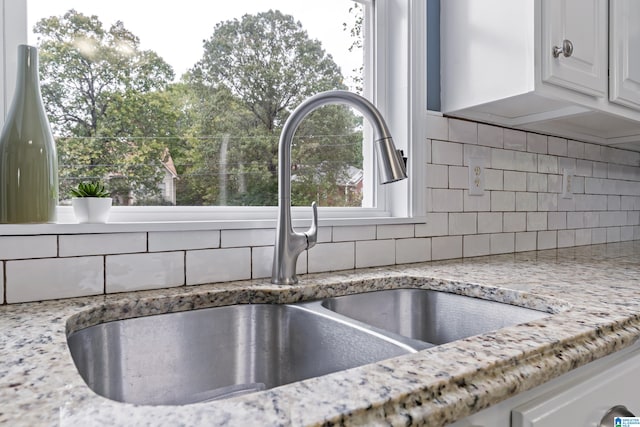 interior details featuring white cabinets, backsplash, light stone counters, and sink