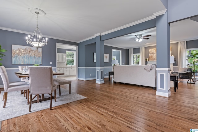 dining space with hardwood / wood-style flooring, ceiling fan with notable chandelier, a healthy amount of sunlight, and crown molding