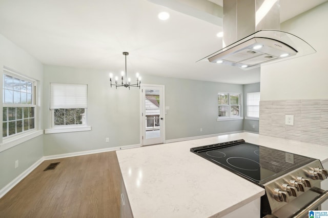 kitchen with island exhaust hood, decorative backsplash, light wood-type flooring, stainless steel range oven, and hanging light fixtures