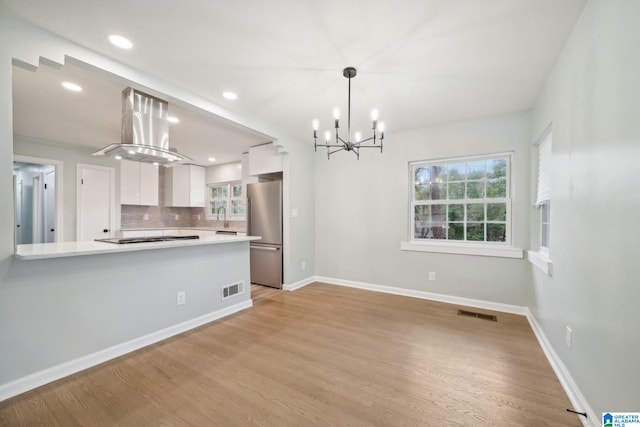 kitchen with decorative backsplash, light hardwood / wood-style floors, white cabinetry, hanging light fixtures, and stainless steel refrigerator