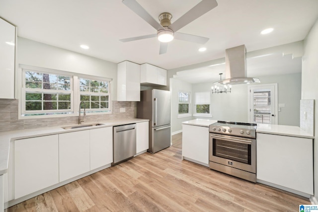 kitchen featuring island exhaust hood, appliances with stainless steel finishes, a healthy amount of sunlight, sink, and white cabinets