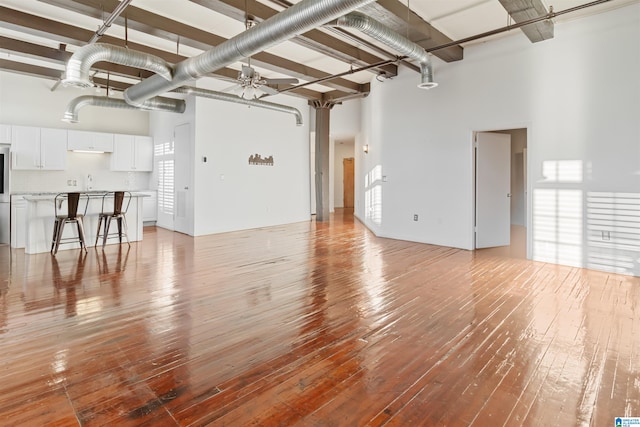 unfurnished living room with ceiling fan, light hardwood / wood-style floors, sink, and a high ceiling