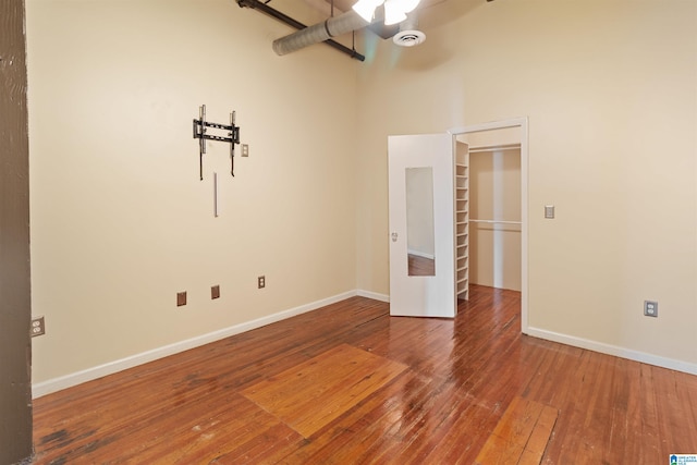 unfurnished bedroom featuring ceiling fan, a closet, a towering ceiling, and hardwood / wood-style flooring