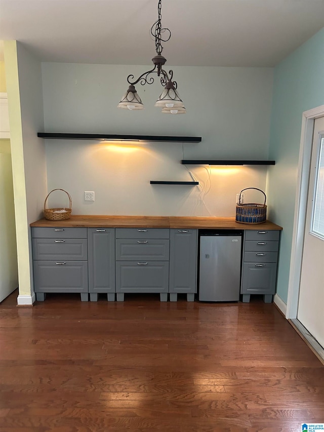 kitchen with gray cabinets, hanging light fixtures, stainless steel refrigerator, and dark wood-type flooring