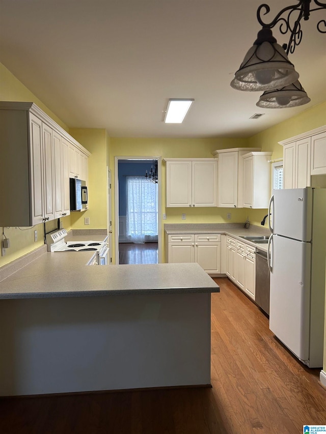 kitchen featuring kitchen peninsula, hanging light fixtures, hardwood / wood-style flooring, white cabinetry, and stainless steel appliances