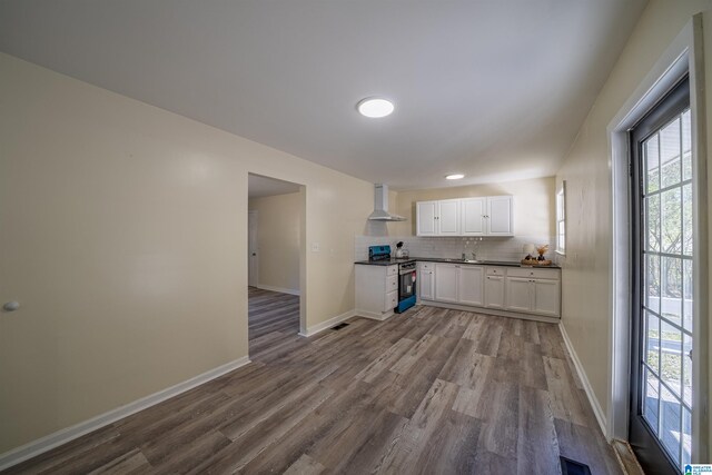 kitchen with white cabinetry, backsplash, hardwood / wood-style floors, stainless steel range oven, and wall chimney exhaust hood