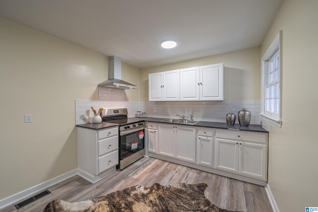 kitchen featuring white cabinetry, stainless steel range oven, sink, and wall chimney range hood