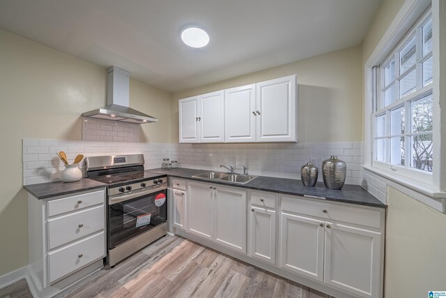 kitchen with wall chimney range hood, sink, white cabinetry, stainless steel range, and light wood-type flooring