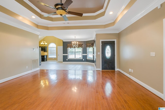 foyer featuring a tray ceiling, light wood-type flooring, ceiling fan with notable chandelier, and ornamental molding