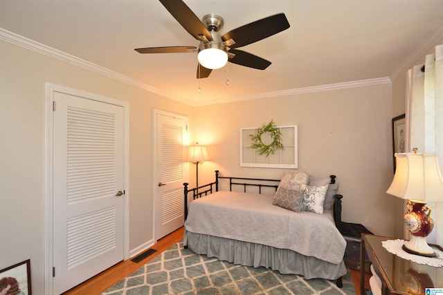 bedroom featuring hardwood / wood-style flooring, ceiling fan, ornamental molding, and two closets