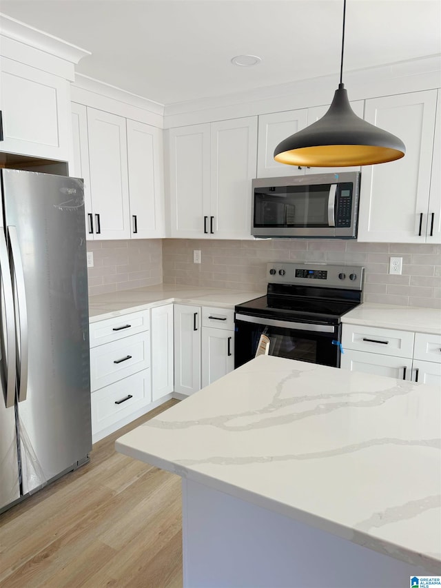 kitchen featuring white cabinets, hanging light fixtures, light wood-type flooring, appliances with stainless steel finishes, and light stone counters