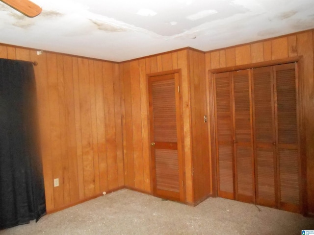 interior space with a closet, light colored carpet, ceiling fan, and wooden walls