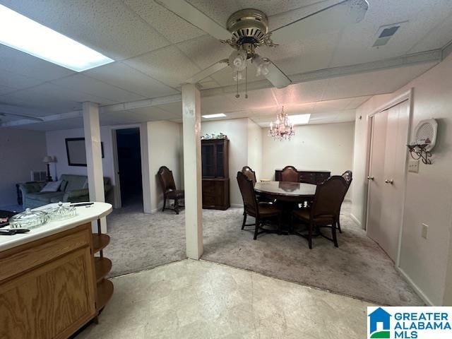 carpeted dining space with a drop ceiling and ceiling fan with notable chandelier