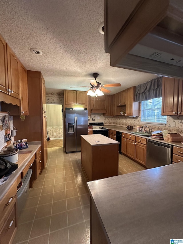 kitchen with a textured ceiling, a kitchen island, stainless steel appliances, sink, and ceiling fan