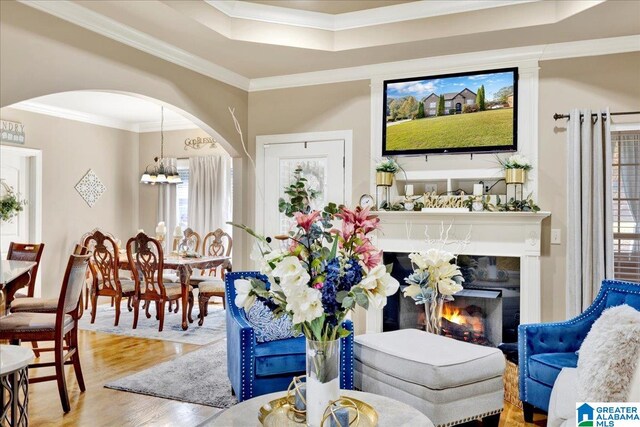 living room with a tray ceiling, a chandelier, wood-type flooring, and ornamental molding