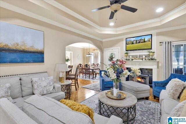 living room featuring ceiling fan, wood-type flooring, ornamental molding, and a tray ceiling